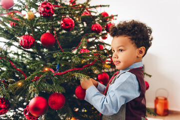 Adorable 3 year old toddler boy decorating Christmas tree