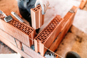 Industrial construction worker using spatula and trowel for building walls with bricks and mortar - obrazy, fototapety, plakaty