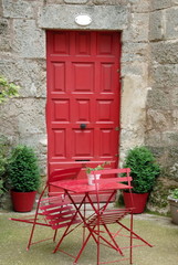 Fototapeta na wymiar Ville de Pézenas, table et chaises rouges devant une porte d'entrée rouge, département de l'Hérault, France