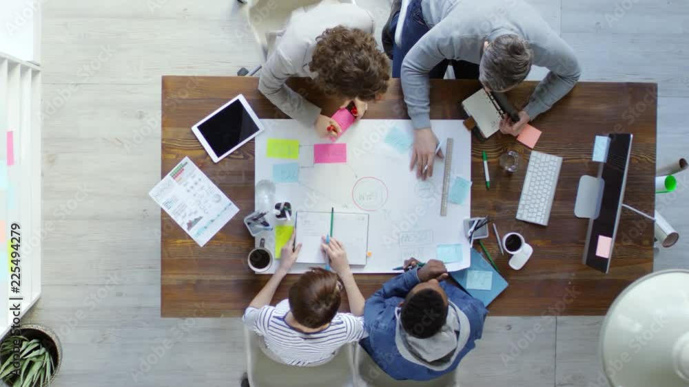 Poster top view of group of four multiethnic business people sitting at desk in office and using sticky not