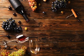 Vintage bottle of red wine with blank matte black label, corkscrew & bunches grapes on wooden table...
