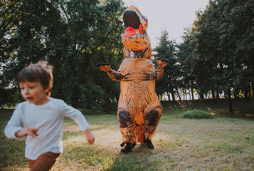 Father and son playing at the park, with a dinosaur costume, having fun with the family outdoor © oneinchpunch