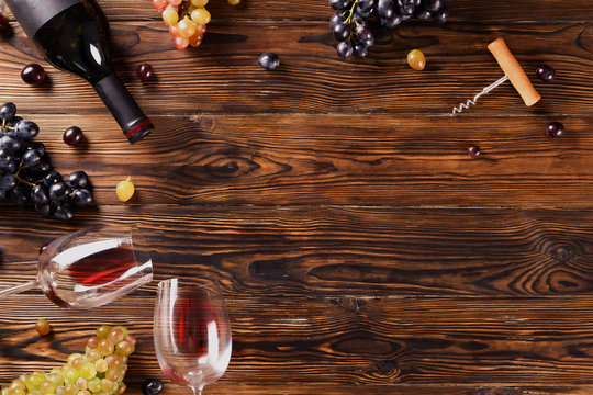 Vintage bottle of red wine with blank matte black label, corkscrew & bunches grapes on wooden table background. Expensive bottle of cabernet sauvignon concept. Copy space, top view, flat lay.