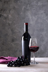 Obraz na płótnie Canvas Vintage bottle of red wine with blank matte black label, bunch of grapes on wooden table, concrete wall background. Expensive bottle of cabernet sauvignon concept. Copy space, top view, flat lay.