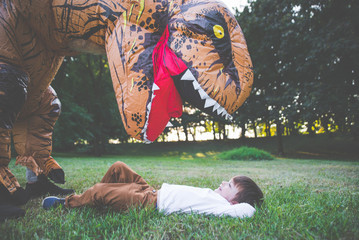 Father and son playing at the park, with a dinosaur costume, having fun with the family outdoor
