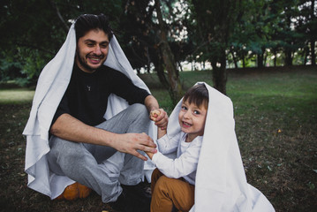 Father and son playing ghosts with white sheets in the garden, conceptual photos about halloween