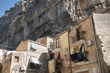 Cefalu, Italy - September 09, 2018: View of old buildings with the Rocca and fortifications high above.