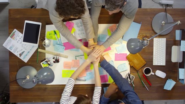 Top view of creative entrepreneurs making stack of hands while celebrating success after hard work in office