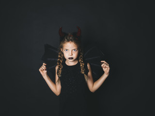 beautiful, blond girl is dressed as halloween devil with red horns and wings