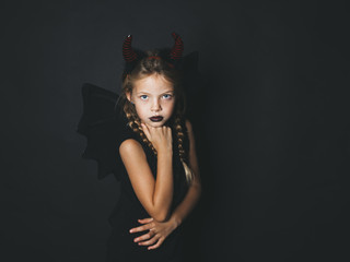 beautiful, blond girl is dressed as halloween devil with red horns and wings