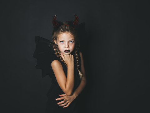 beautiful, blond girl is dressed as halloween devil with red horns and wings