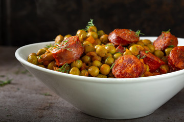 Stew made from green peas, carrot and pork sausages in a white bowl