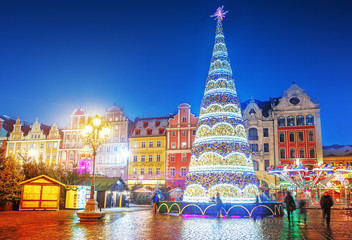 Wroclaw, Poland, Christmas market square and illuminated Christmas tree in the center of old city. New Year ambiance, illuminated and ornamented festive city. Night scene. - obrazy, fototapety, plakaty
