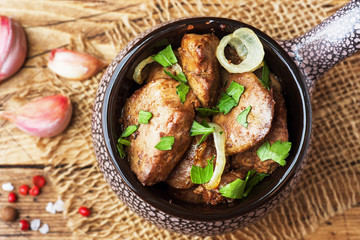 Baked chicken liver with onion in a ceramic cocotte on a wooden rustic table.