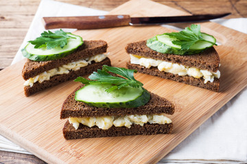 Sandwich with scrambled eggs, cucumbers and parsley on wooden rustic background.