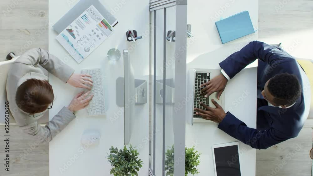 Poster top view of two multiethnic office workers, man and woman, sitting at desks opposite each other and 
