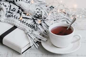 Red hibiscus tea in a white cup, white book (or diary, planner), lights on wooden background. Tea break concept. Hygge style