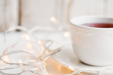 Cup with red hibiscus tea and yellow lights for home decoration. Cosy atmosphere