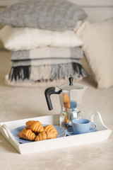 Breakfast in bed. On a white tray there is a coffee maker, coffee blue cup and croissants.