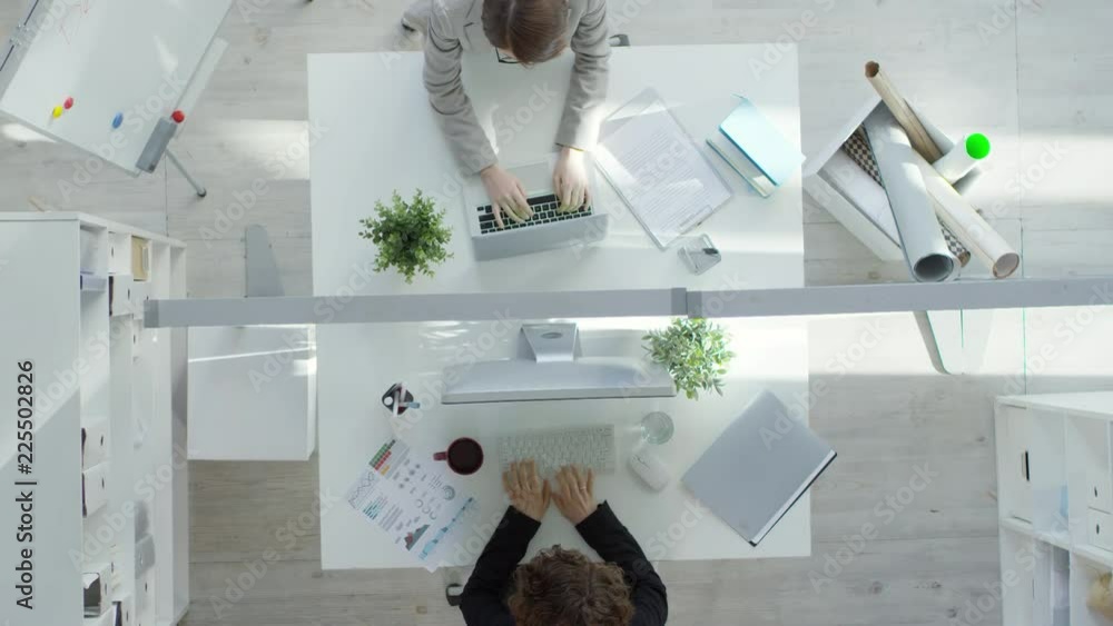 Poster top view of two female colleagues sitting opposite each other in modern office and using laptop and 