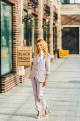 beautiful stylish woman holding shopping bag with black friday sign and looking up at mall