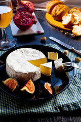 Camembert cheese on a black plate with figs, pistachios and wine in a glass, cut garnet on marble stone, fresh bread