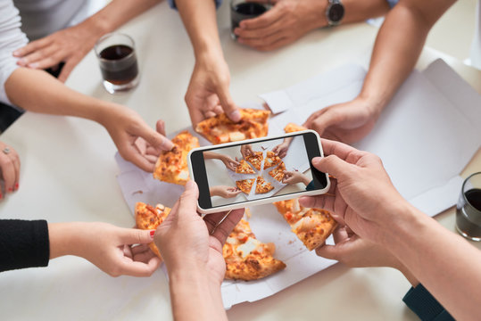 Young man taking photo of pizza and soft drink with smart phone