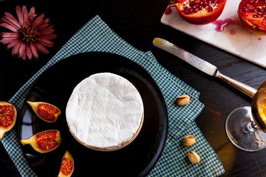 Camembert cheese on a black plate with figs, pistachios and wine in a glass, cut garnet on marble stone, top view