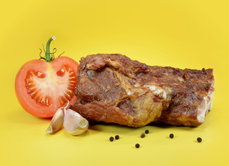 Smoked pork ribs with half tomato, black pepper and garlic on a yellow background