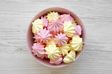 Mini meringues in a pink bowl over white wooden background, top view. Flat lay, overhead, from above.