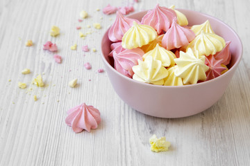 Fototapeta na wymiar Mini meringues in a pink bowl over white wooden background, side view. Close-up.