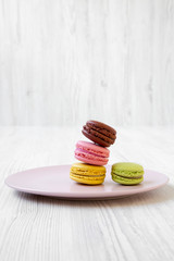Sweet and colorful macarons on pink plate over white wooden surface, side view. Close-up.