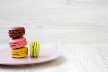 Sweet and colorful macarons on pink plate over white wooden background, side view. Close-up. Copy space.
