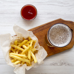 French fries, ketchup and cold beer on a white wooden table, view from above. Top view, overhead. Close-up.