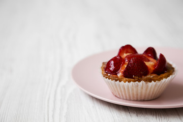 Strawberry vanilla cream cheese tart on pink plate, side view. Close-up. White wooden surface. Copy space.