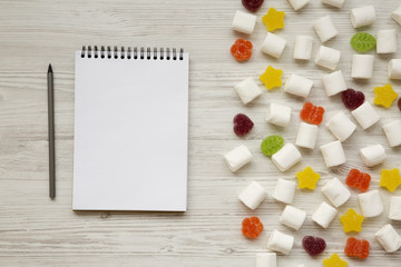 Candy and blank notepad with pencil on a white wooden background, top view. From above, flat lay,...