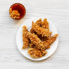 Spicy chicken fingers on white plate with sauce over white wooden background, top view. Flat lay, from above, overhead. Closeup.