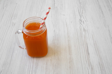 Glass jar of carrot smoothie on white wooden background, low angle view. Copy space.