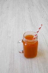 Carrot smoothie in glass jar over white wooden background, low angle view. Close-up. Copy space.