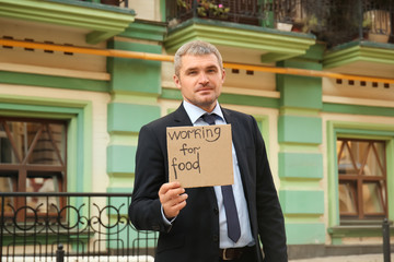 Businessman holding piece of cardboard with text WORKING FOR FOOD outdoors