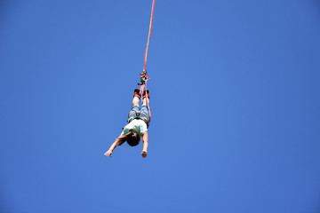 Naklejka na ściany i meble Bungee jumping from crane. Seen from the ground young woman hanging on a cord high in the blue sky