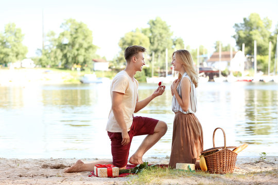 Young man making proposal to his girlfriend on romantic date near river