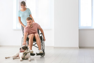 Young man in wheelchair with his wife and service dog at home