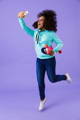 African girl posing isolated over violet background holding skateboard take a selfie by phone.