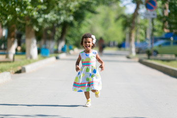 Black girl runs on the asphalt. Dark-skinned little girl running along the road in the yard.