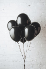 bunch of black balloons on ribbons in front of white brick wall