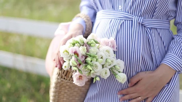 Close up view of pregnant belly in nature. Woman hold bouquet and caress her belly