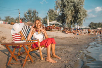 Fototapeta na wymiar Girl talking on a phone and drinking juice on the beach