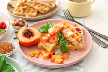 Plate with delicious waffles and peach slices on table