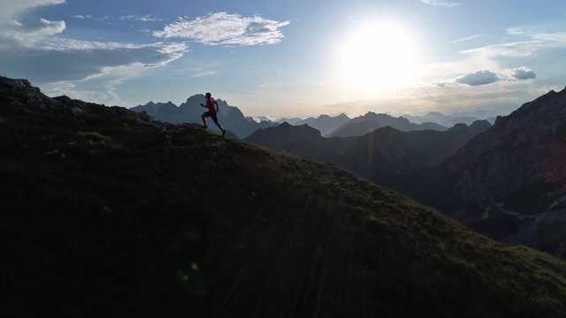 Aerial - Young sportsman running uphill on the edge of the mountain at sunset